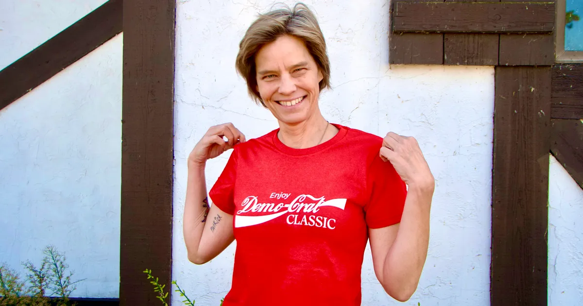 Becka Thompson wearing a red Demo-Crat Classic T-shirt, a playful nod to the 1985 “New Coke” campaign, symbolizing her call to restore classic Democratic competence in Minneapolis.